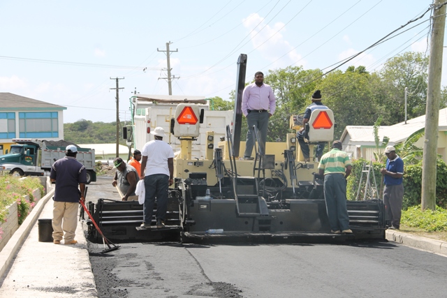 Junior Minister in the Ministry of Communications and Works Hon. Troy Liburd (standing on the asphalt paver) oversees final road works on the Charlestown Bypass. The road has since been renamed Stuart Williams Drive